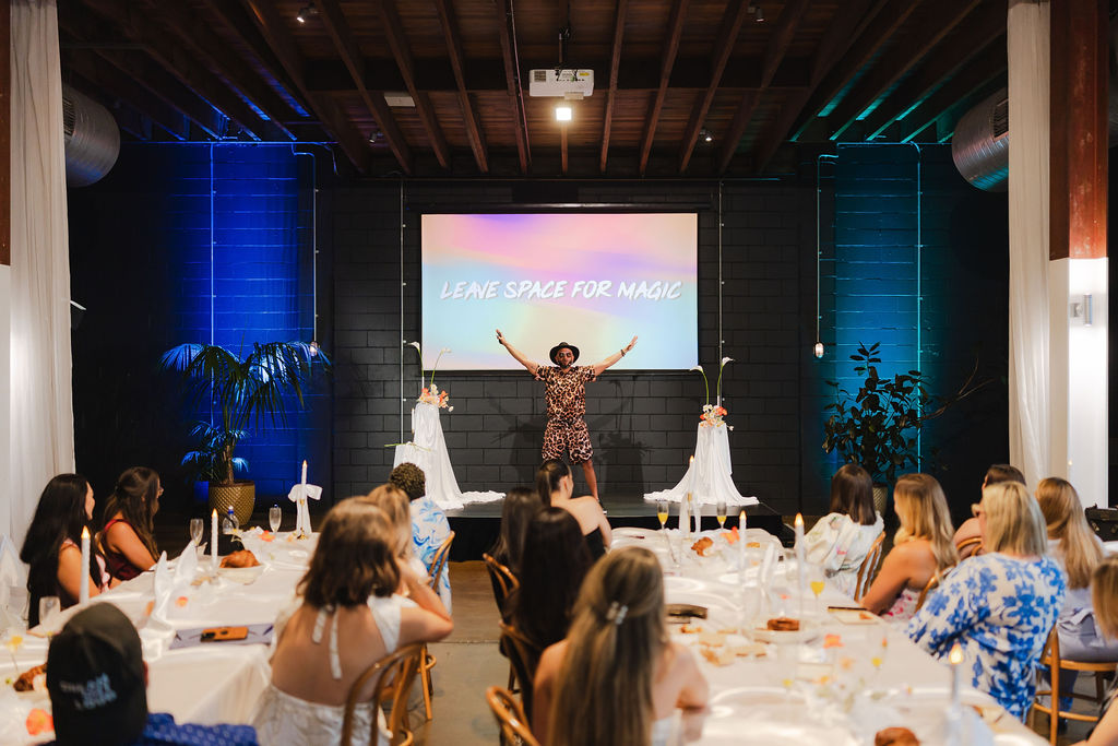 A speaker welcoming seated guests with arms outstretched