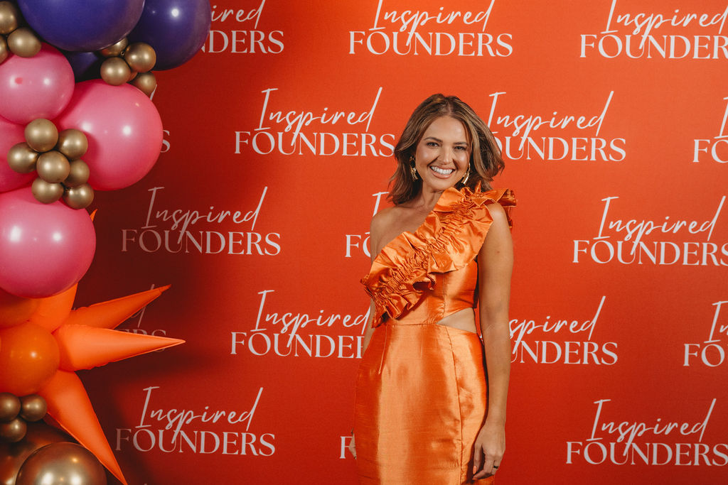 A guest smiling on the Inspired Founders step and repeat beside the balloon arch